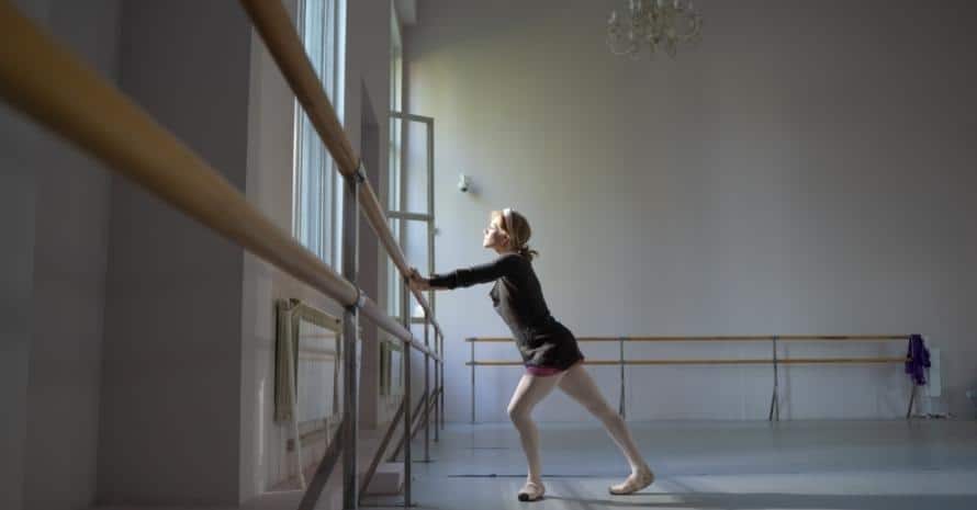 A woman does ballet while holding on to a barre